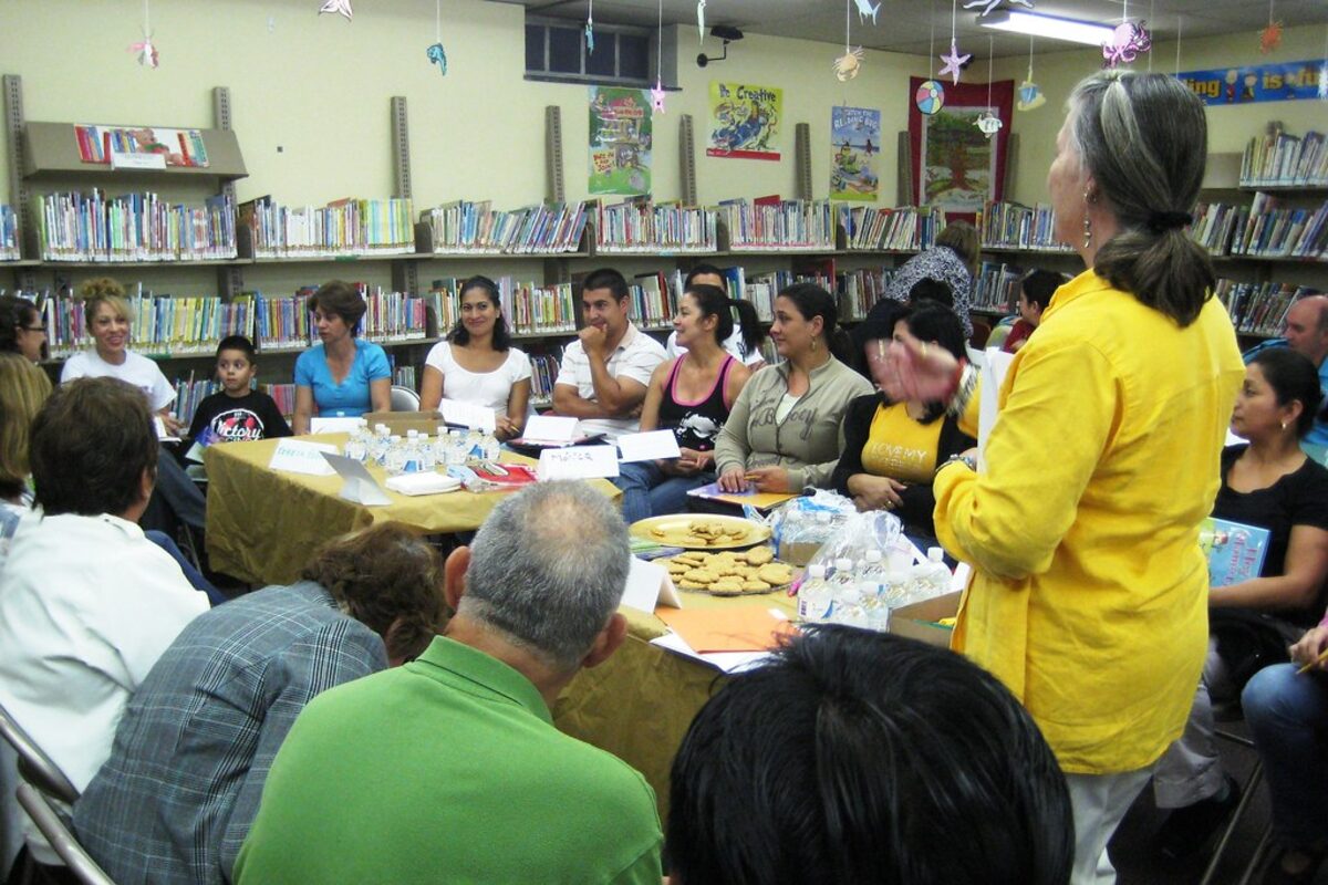 Adult language learners around a table in a classroom.