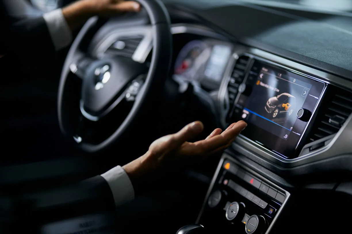 Hand reaching for the central touchscreen of a car dashboard.