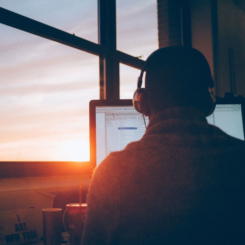 A learner wearing headphones at a desk by a window at sunrise.